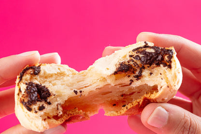 Hands holding a split mochi bread against a pink background