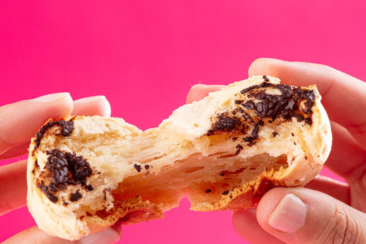 Hands holding a split mochi bread against a pink background